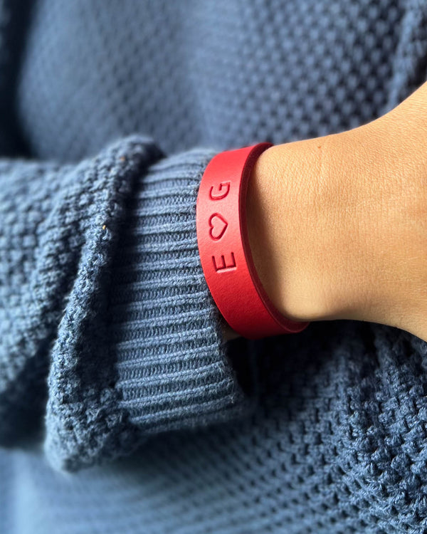 MONO Lederarmband in Rot mit gravierten Initialen "E ♡ G" am Handgelenk, getragen zu blauem Strickpullover