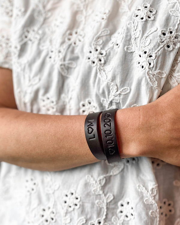 DUO Lederarmband in Dunkelbraun mit den Gravuren "L ♡ M" und "♡ 10.10.20 ♡" am Handgelenk, weiße bestickte Bluse