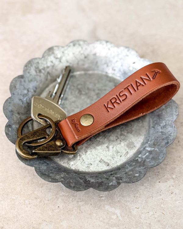 HOOK Schlüsselanhänger aus cognacfarbenem Leder mit der Gravur "KRISTIAN" und Flugzeugsymbol, mit Schlüssel in einer Metallschale