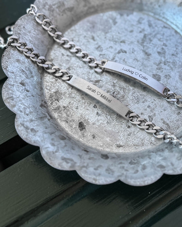 ARA Armband aus silberfarbenem Edelstahl, matte Platte mit "Sarah ♡ Mikkel" und glänzende Platte mit "Ludvig ♡ Colin" graviert, auf Zinkschale