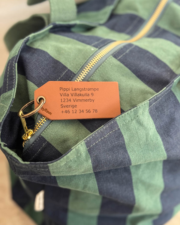 ATLAS Kofferanhänger aus Leder, hier in Cognac, graviert mit Adresse für "Pippi Langstrømpe" auf gestreifter Reisetasche