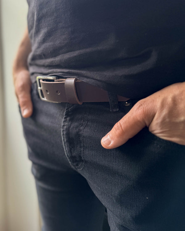 EDGE Gürtel aus dunkelbraunem Leder, getragen zu schwarzer Jeans mit schwarzem T-Shirt und Hand in der Tasche