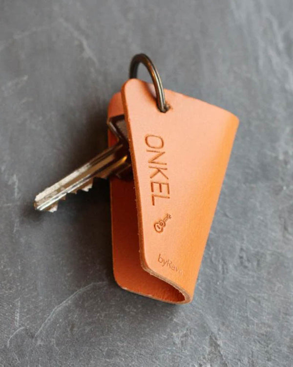 FOLD Schlüsseletui aus Cognac-Leder mit der Gravur "Onkel" und kleiner Gitarre, mit Schlüsseln auf dunklem Schiefer