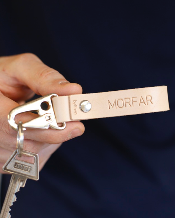 HOOK Schlüsselanhänger aus naturfarbenem Leder mit Karabiner aus Stahl und der Gravur "Morfar", in der Hand gehalten mit Schlüssel