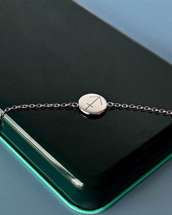 IBI STAR Armband aus silberfarbenem Edelstahl mit Sternzeichen Schütze auf runder Platte graviert, auf dunkelgrüner Schachtel liegend