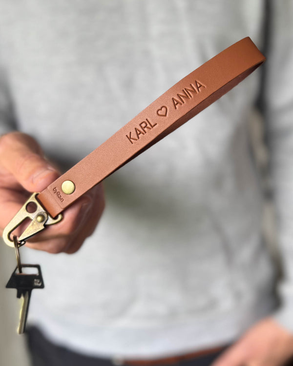 IRON Schlüsselanhänger aus Cognac-Leder mit den gravierten Namen "Karl ♡ Anna", in der Hand gehalten mit Schlüssel