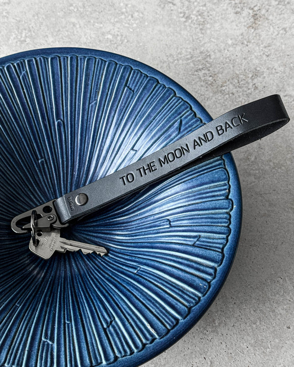 IRON Schlüsselanhänger aus schwarzem Leder mit der Gravur "To the moon and back" und Schlüsseln in blauer geriffelter Keramikschale
