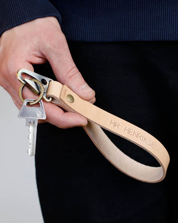 IRON Schlüsselanhänger aus naturfarbenem Leder mit langer Handschlaufe und der Gravur "Hr. Henriksen", in der Hand gehalten mit Schlüssel