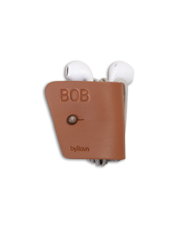 KAX Kopfhörerhalter von byRavn aus Cognac-Leder mit Gewehrknopf in Antikmessing und dem gravierten Namen "Bob", mit Earpods
