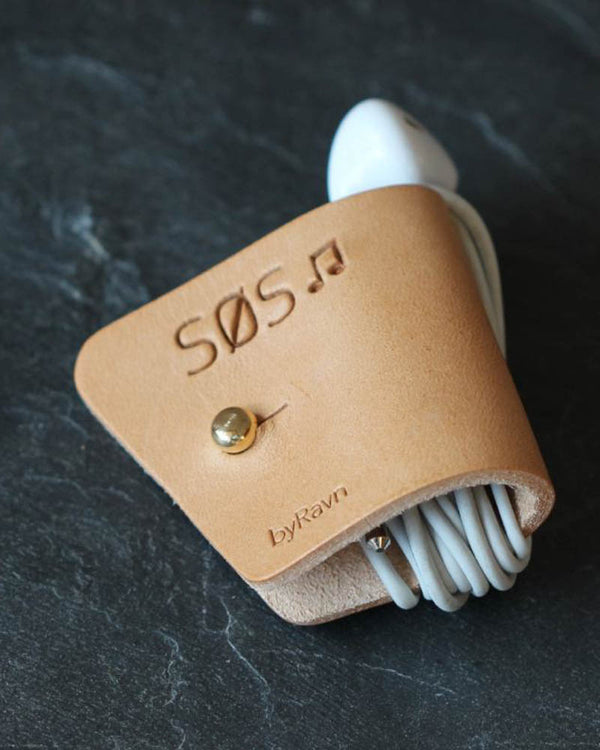 KAX Kopfhörerhalter aus naturfarbenem Leder mit der Gravur "Søs" ♪ und Messingknopf, mit Earpods auf dunklem Schiefer