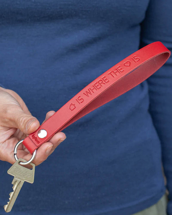 LUX Schlüsselanhänger aus rotem Leder mit der Gravur "Home is where the heart is" mit Haus- und Herzsymbol, in der Hand gehalten