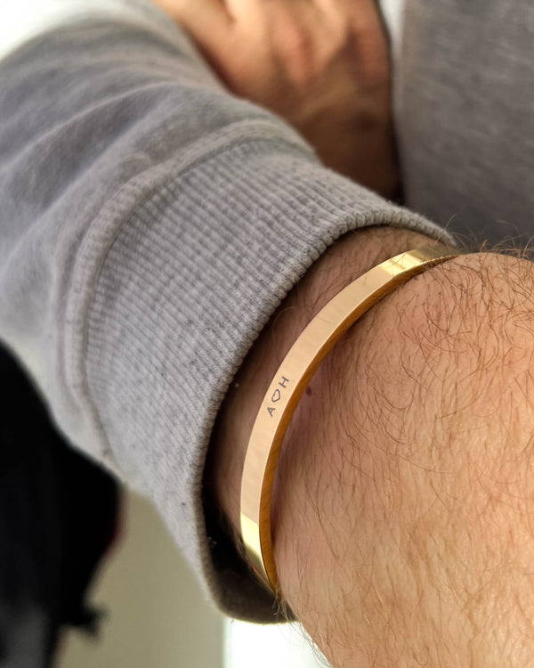 MARS Armband aus vergoldetem Edelstahl mit gravierten Initialen "A ♡ H" am Handgelenk eines Mannes, graues Sweatshirt