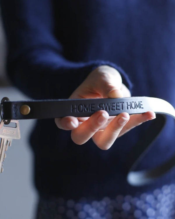 MAX Schlüsselanhänger aus schwarzem Leder als lange Schlaufe mit persönlicher Gravur "Home sweet home", in der Hand gehalten mit Schlüsseln
