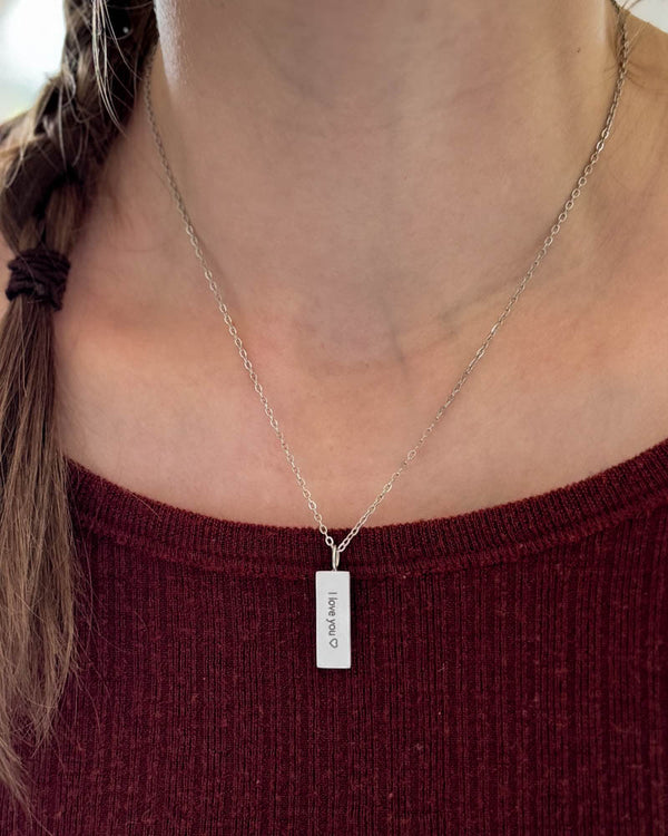 MIO Halskette aus silberfarbenem Edelstahl mit Gravur "I love you" ♡ auf rechteckigem Anhänger, um den Hals getragen über bordeauxrotem Top