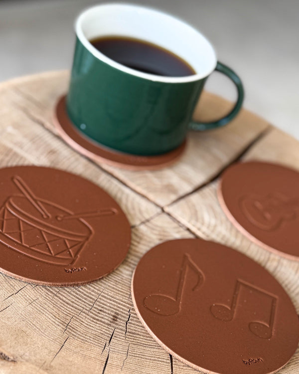 MOKKA Untersetzer aus cognacfarbenem Leder, geprägt mit Trommel und Noten, auf Holzscheibe mit grüner Kaffeetasse