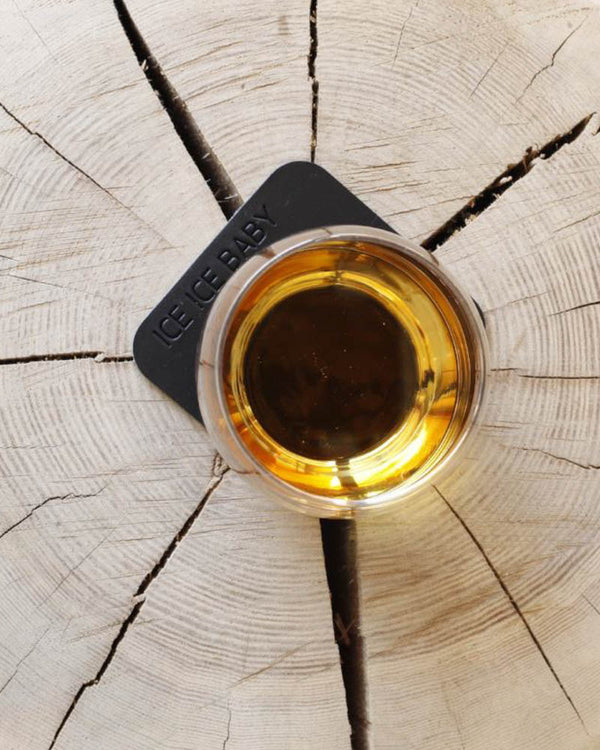 MOKKA quadratischer Untersetzer aus schwarzem Leder mit der Gravur "Ice ice baby" unter Whiskyglas auf Holzscheibe, von oben