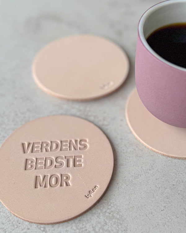 MOKKA Untersetzer aus naturfarbenem Leder mit Prägung "Verdens bedste mor" auf hellem Tisch mit rosa Kaffeetasse