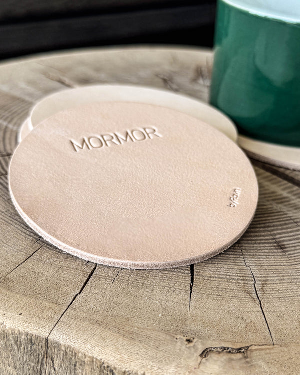 MOKKA runde Untersetzer aus naturfarbenem Leder mit der Gravur "Mormor" auf Holzscheibe neben grüner Tasse