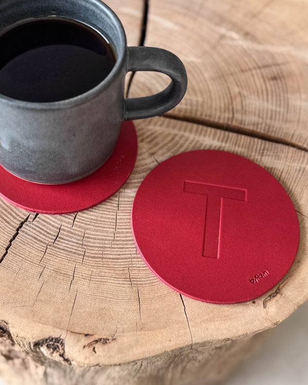 MOKKA Untersetzer aus rotem Leder mit geprägtem Buchstaben "T" auf Holzscheibe neben grauer Kaffeetasse auf Untersetzer