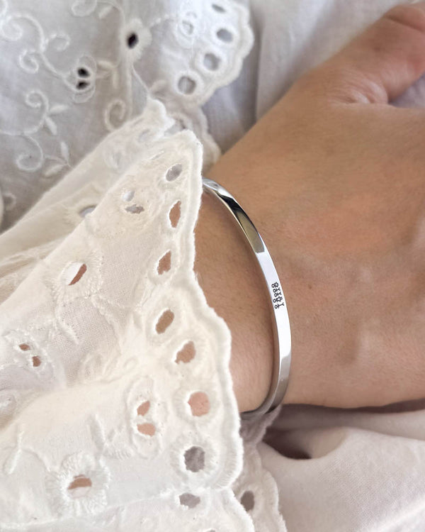 VENUS STICK Armband aus silberfarbenem Edelstahl mit gravierter Streichholz-Familie, getragen zu weißer Bluse mit Stickerei