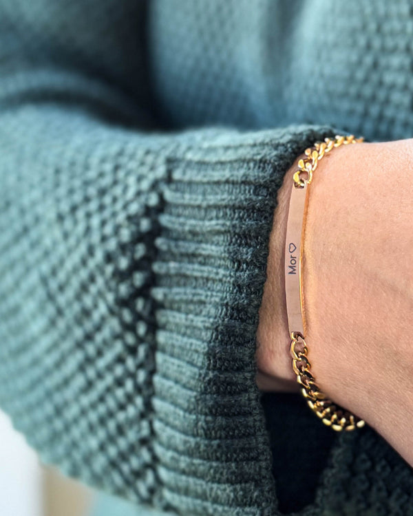 ZOE Armband aus vergoldetem Edelstahl mit der Gravur "Mor" ♡ auf länglicher Platte, am Handgelenk zu grünem Strick getragen
