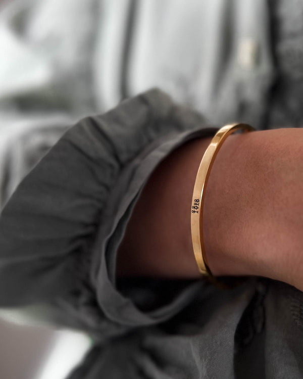 VENUS STICK Armband aus vergoldetem Edelstahl mit gravierter Streichholz-Familie, am Handgelenk zu grauer Bluse