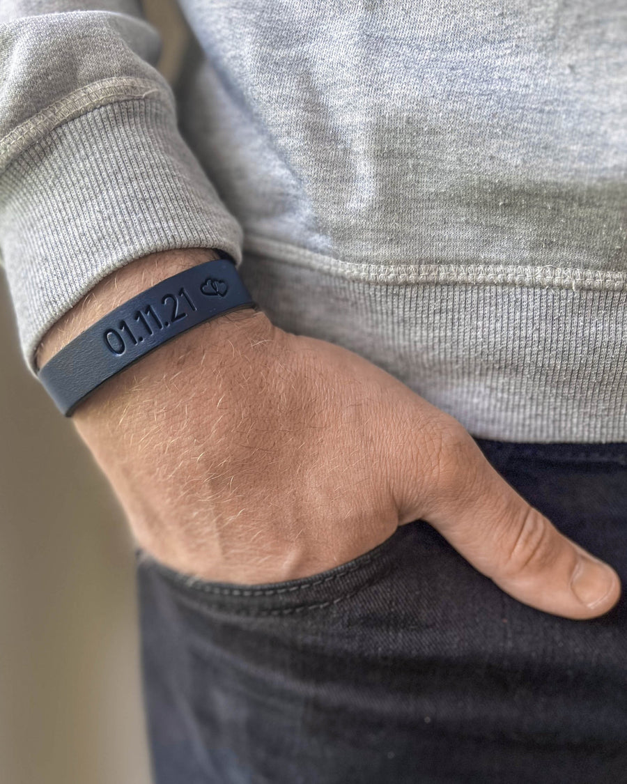 MONO Lederarmband in Dunkelblau mit graviertem Datum "01.11.21" und kleinem Symbol am Handgelenk, Hand in der Tasche