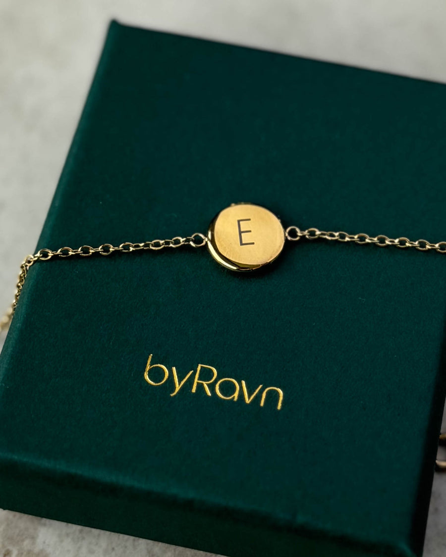 IBI LETTER Armband aus vergoldetem Edelstahl mit graviertem Buchstaben "E", auf dunkelgrüner byRavn Schmuckschachtel