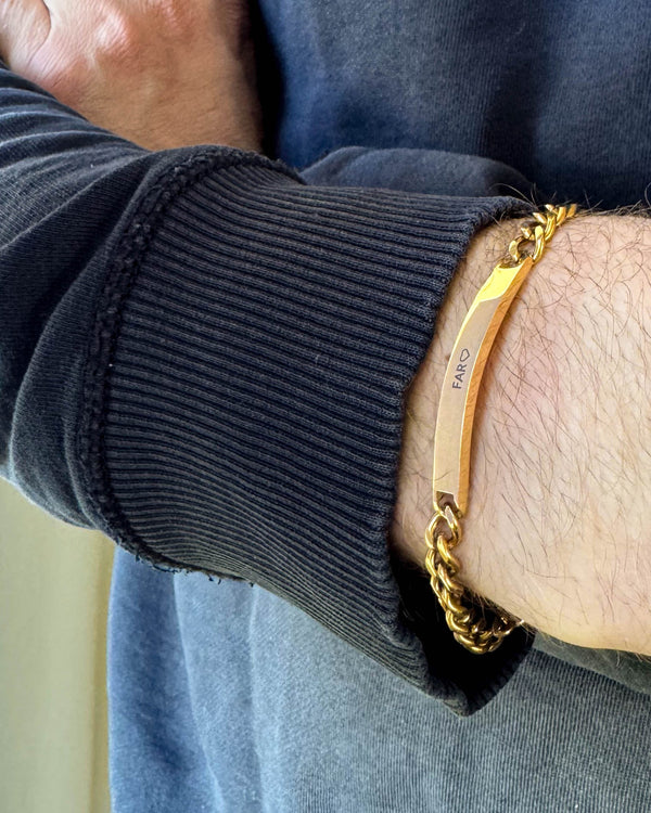 ARA Armband aus vergoldetem Edelstahl mit der Gravur "Far" ♡ am Handgelenk eines Mannes, schwarzes Sweatshirt