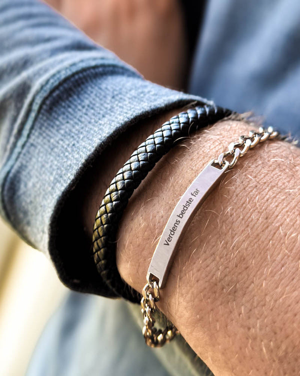 ARA Armband aus silberfarbenem Edelstahl mit der Gravur "Verdens bedste far" am Handgelenk, kombiniert mit geflochtenem RAY Lederarmband