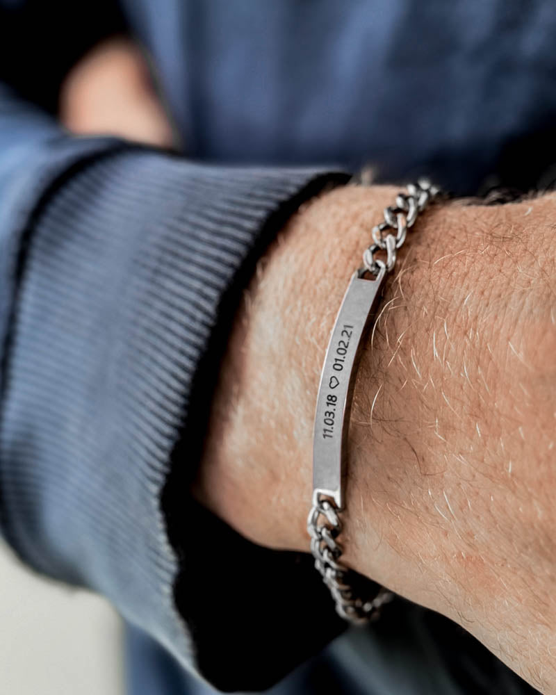 ARA Armband aus silberfarbenem Edelstahl mit den Daten "11.03.18 ♡ 01.02.21" graviert, am Handgelenk eines Mannes, blaues Sweatshirt