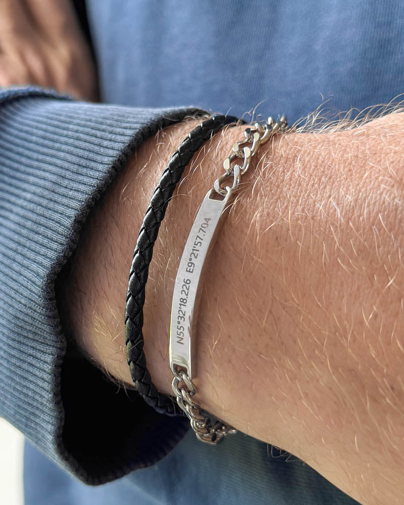 ARA Armband aus silberfarbenem Edelstahl mit den Koordinaten "N55°32'18.226 E9°21'57.704" graviert, mit schwarzem geflochtenem Lederarmband