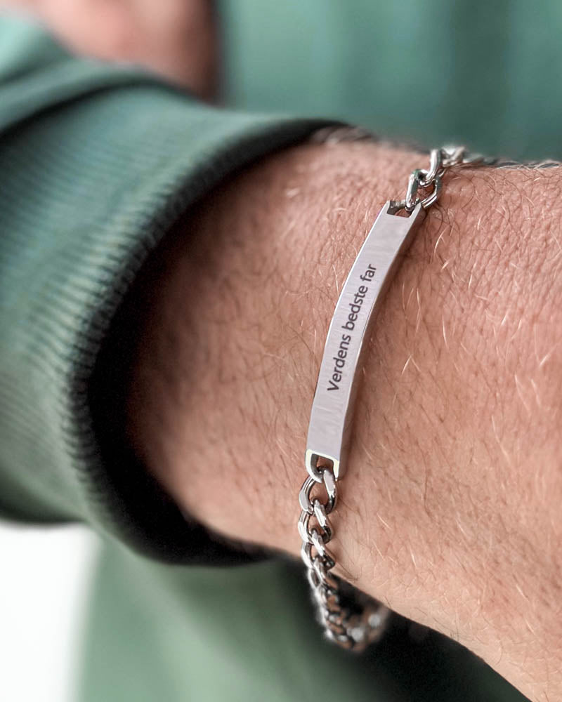 ARA Armband aus silberfarbenem Edelstahl mit der Gravur "Verdens bedste far" am Handgelenk eines Mannes, grünes Sweatshirt