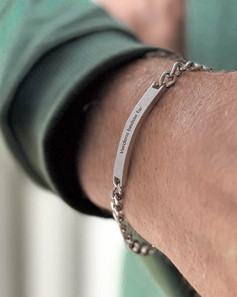 ARA Armband aus silberfarbenem Edelstahl mit "Verdens bedste far" auf länglicher Platte graviert, schräg am Handgelenk gezeigt