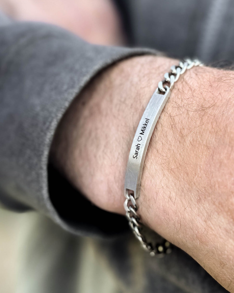 ARA Armband aus gebürstetem silberfarbenem Edelstahl mit Gravur "Sarah ♡ Mikkel", am Handgelenk eines Mannes getragen