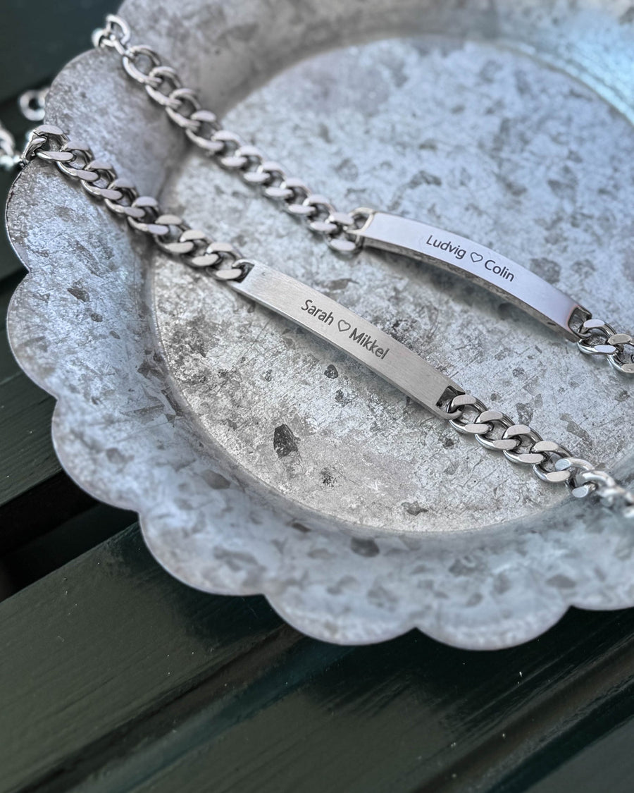 ARA Armband aus silberfarbenem Edelstahl, zwei Stück graviert mit "Ludvig ♡ Colin" und "Sarah ♡ Mikkel", auf Zinkschale liegend