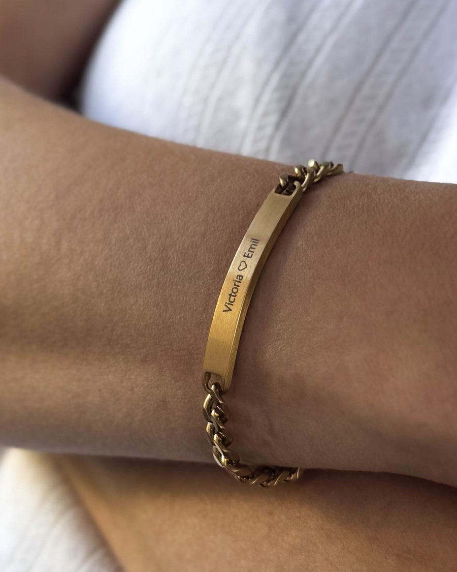 AVA Armband aus gebürstetem vergoldetem Edelstahl mit persönlicher Gravur "Victoria ♡ Emil", am Handgelenk getragen