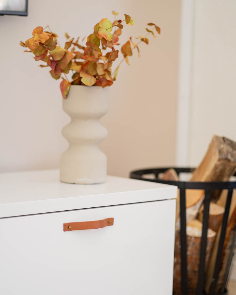 BAND Ledergriff in Cognac an weißer Kommode mit beiger Vase mit Herbstzweigen und Holzkorb daneben