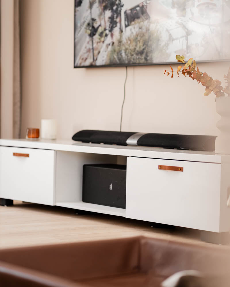 BAND Ledergriffe in Cognac an weißem TV-Board mit zwei Schubladen, Soundbar und Fernseher an der Wand im Wohnzimmer