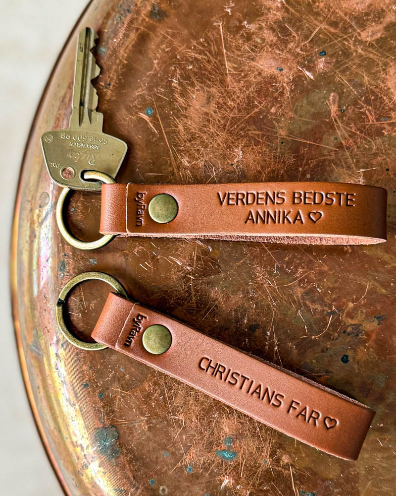 Zwei BOND Schlüsselanhänger aus Cognac-Leder mit "Verdens bedste Annika" ♡ und "Christians far" ♡ graviert, auf Kupfertablett mit Schlüssel