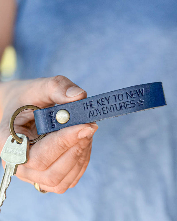 BOND Schlüsselanhänger aus dunkelblauem Leder mit persönlicher Gravur "The key to new adventures" ☆, in der Hand gehalten mit Schlüssel