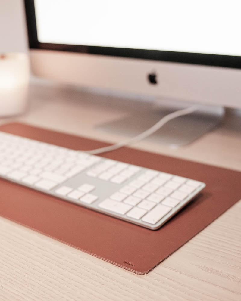 DESK Schreibtischunterlage aus cognacfarbenem Leder unter weißer Tastatur vor iMac auf hellem Holzschreibtisch