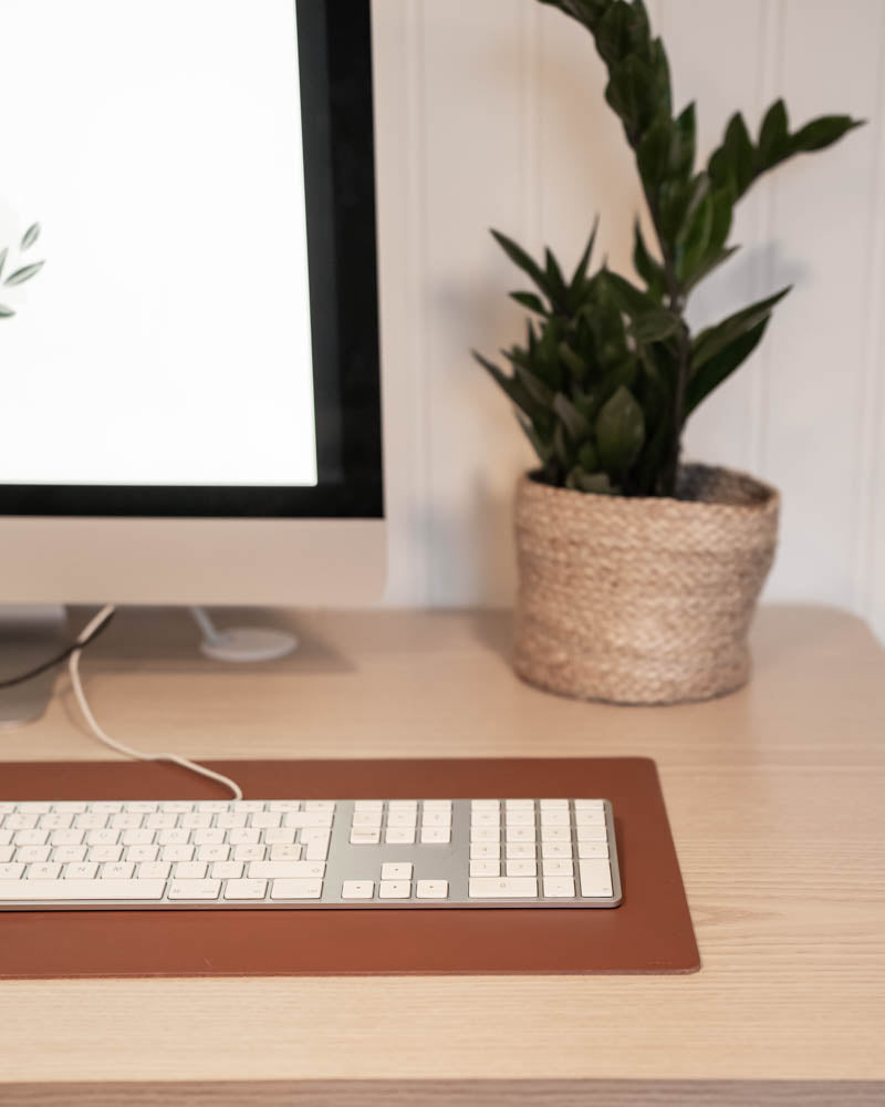 DESK Schreibtischunterlage aus cognacfarbenem Leder mit Tastatur vor iMac und grüner Pflanze im Korb auf hellem Schreibtisch