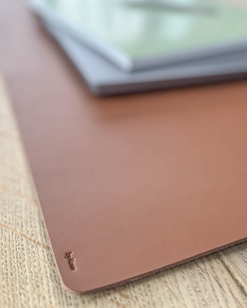 DESK Schreibtischunterlage aus cognacfarbenem Leder, Nahaufnahme der Ecke mit byRavn-Prägung unter Laptop auf Holztisch