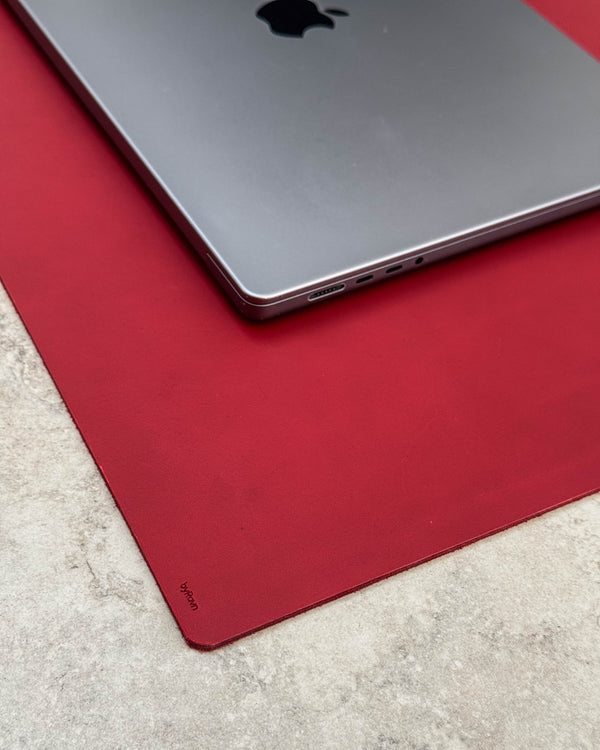 DESK Schreibtischunterlage aus rotem Leder mit byRavn-Prägung unter silberfarbenem Laptop auf heller Tischplatte