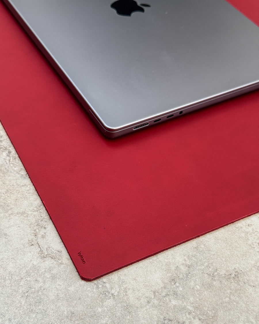 DESK Schreibtischunterlage aus rotem Leder mit byRavn-Prägung unter silberfarbenem Laptop auf heller Tischplatte
