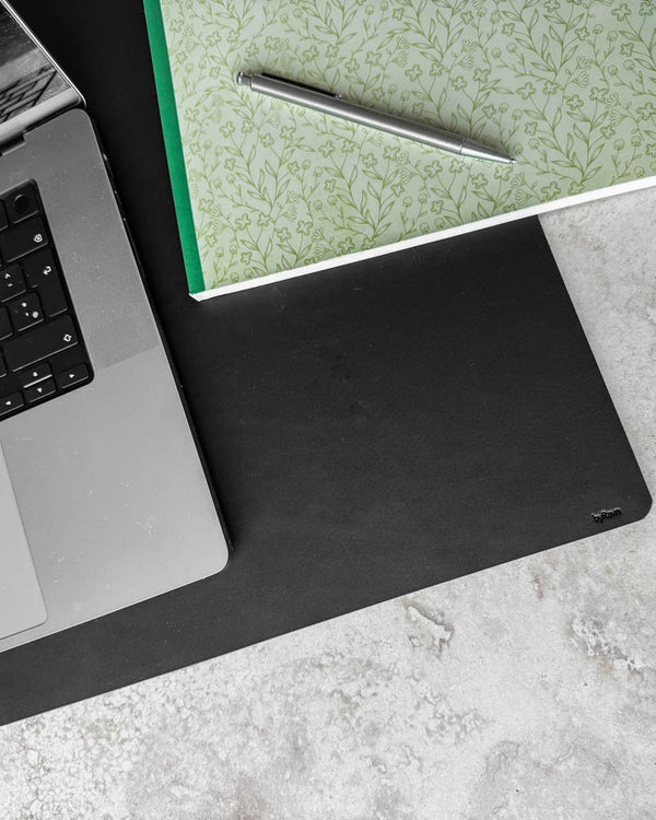 DESK Schreibtischunterlage aus schwarzem Leder von oben mit Laptop, geblümtem Notizbuch und Kugelschreiber auf heller Tischplatte