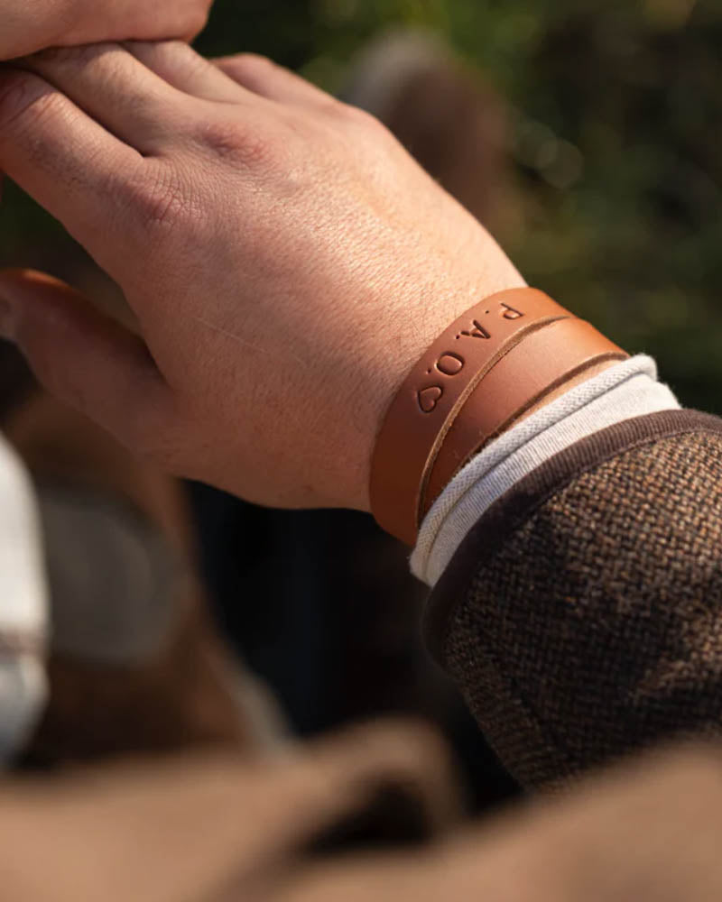 DUO Lederarmband in Cognac mit gravierten Initialen "P.A.O." ♡, am Handgelenk getragen im Freien bei Sonnenschein