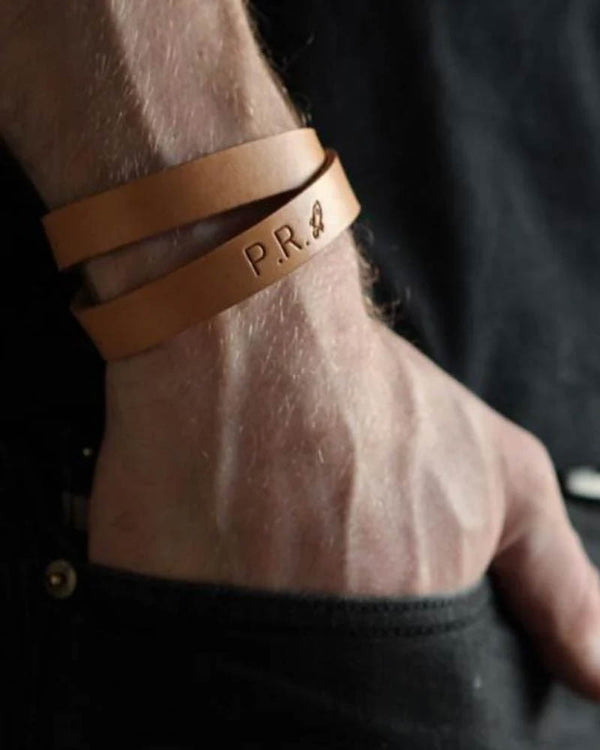 DUO Lederarmband, hier in hellem Cognac gezeigt, mit gravierten Initialen "P.R." und kleinem Motiv am Handgelenk eines Mannes
