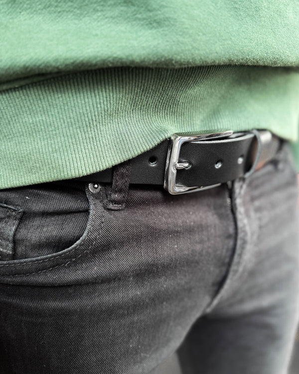 EDGE Gürtel aus schwarzem Leder mit silberfarbener Stahlschnalle, getragen zu schwarzer Jeans mit grünem Sweatshirt